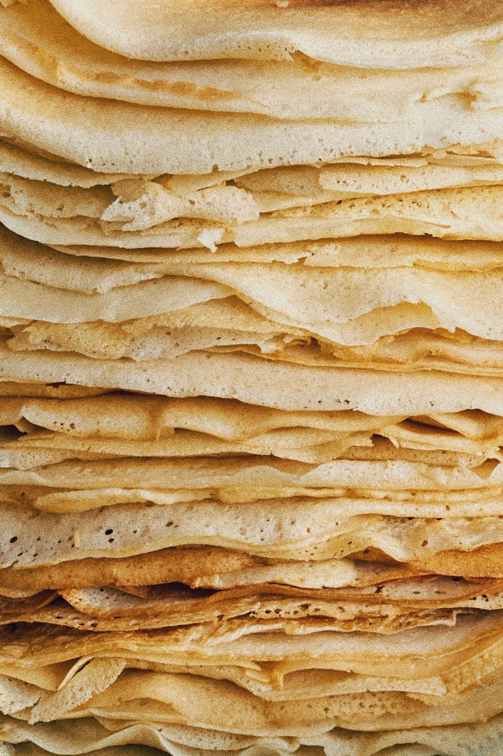 A close-up view of a stack of golden crêpes, showcasing the texture and layers of this classic breakfast dish.